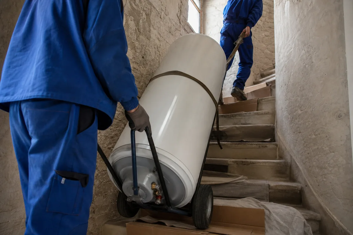 Escalier étroit d’une maison ancienne en pierre avec un ballon d’eau chaude sanglé sur un diable