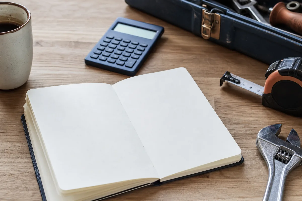 Carnet de devis, calculatrice et clé à molette posés près d’une caisse à outils